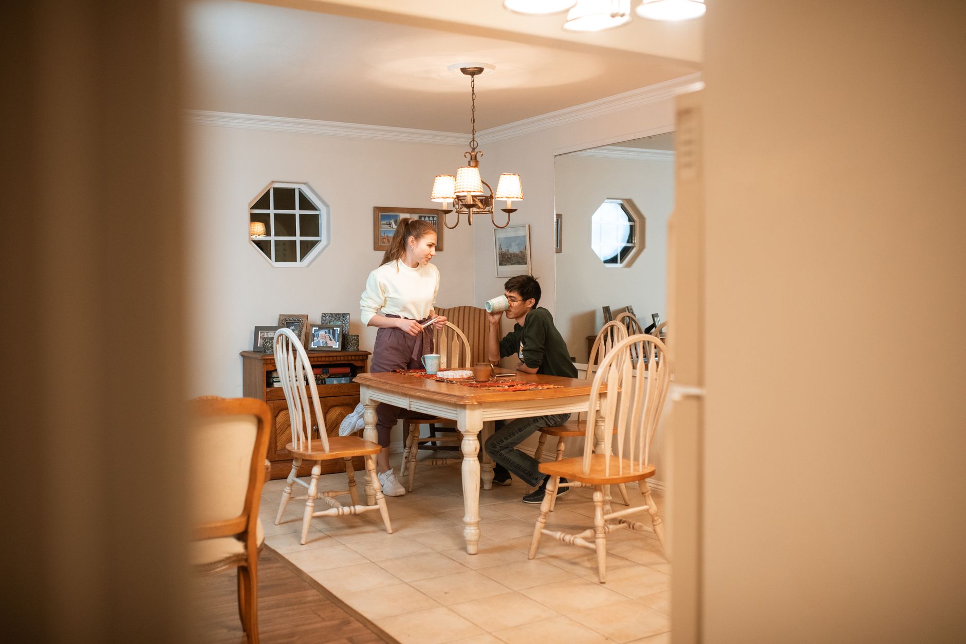 Een jong stel in de eetkamer: hij zit aan tafel met een mok, zij staat ernaast en kijkt naar hem